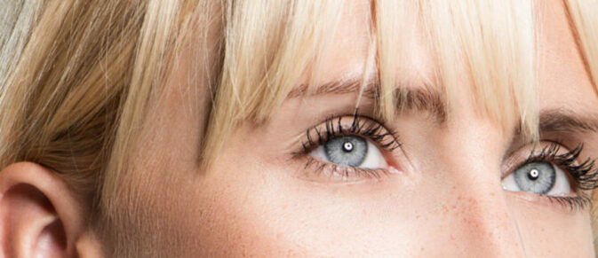 Nahaufnahme eines Gesichts mit blauen Augen und blondem Pony, die direkt nach vorne blicken.